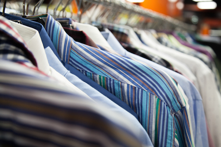 Hangers with colorful male shirts in fashion mall, close up. Shallow depth of field, focus on striped garment